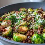 Tender Brussels sprouts and seasoned ground turkey finished with fresh parsley and a lemon wedge on a rustic wooden board.