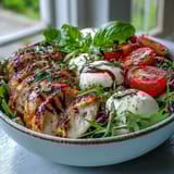 A close-up of a Caprese Chicken Bowl featuring balsamic reduction drizzled over vibrant greens and juicy tomatoes.