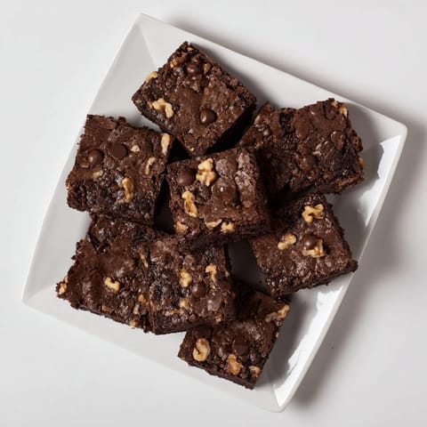Square of fudgy brownie on a white plate next to a tall glass of milk, perfect for an indulgent dessert.