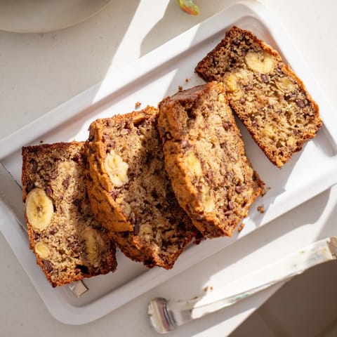 Freshly baked Banana Bread loaf topped with walnuts beside a steaming mug of coffee.