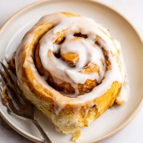 Freshly baked cinnamon rolls cooling on a wire rack, covered in a creamy vanilla glaze and served on a rustic wooden board.