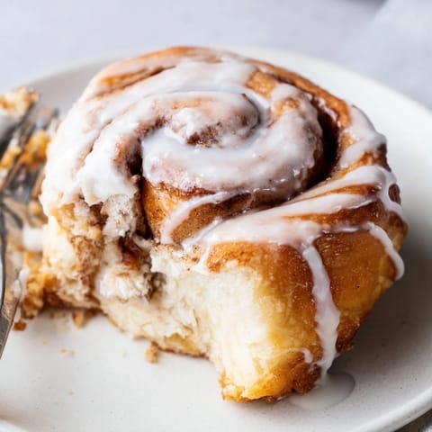Warm cinnamon rolls with gooey brown sugar filling and dripping glaze on a white plate, perfect for a cozy breakfast.