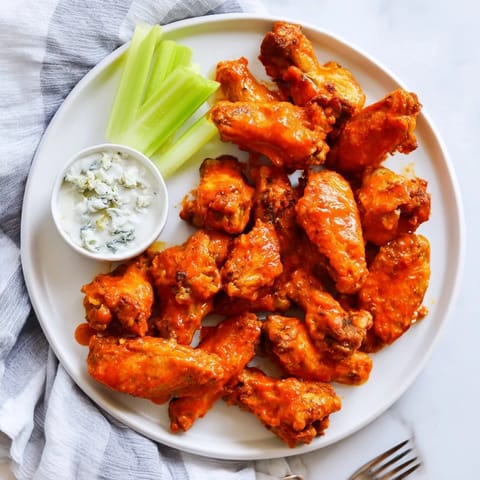 Close-up of saucy Buffalo Wings tossed in tangy red sauce, served with cool dip and celery.