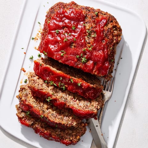 Classic homemade Meatloaf topped with glossy ketchup glaze, sliced thick and served on a plate with creamy mashed potatoes and green beans.