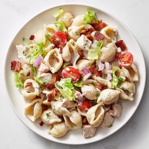 A hearty bowl of BLT Chicken Pasta Salad, featuring tender shells, juicy tomatoes, and fresh greens on a rustic plate.  