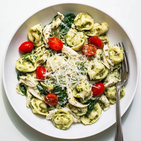 A close-up view of the creamy pesto tortellini skillet, garnished with fresh basil and Parmesan cheese.  